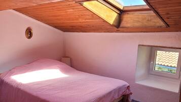 Una habitación pequeña y acogedora con techo inclinado, una cama individual, una ventana y un tragaluz.