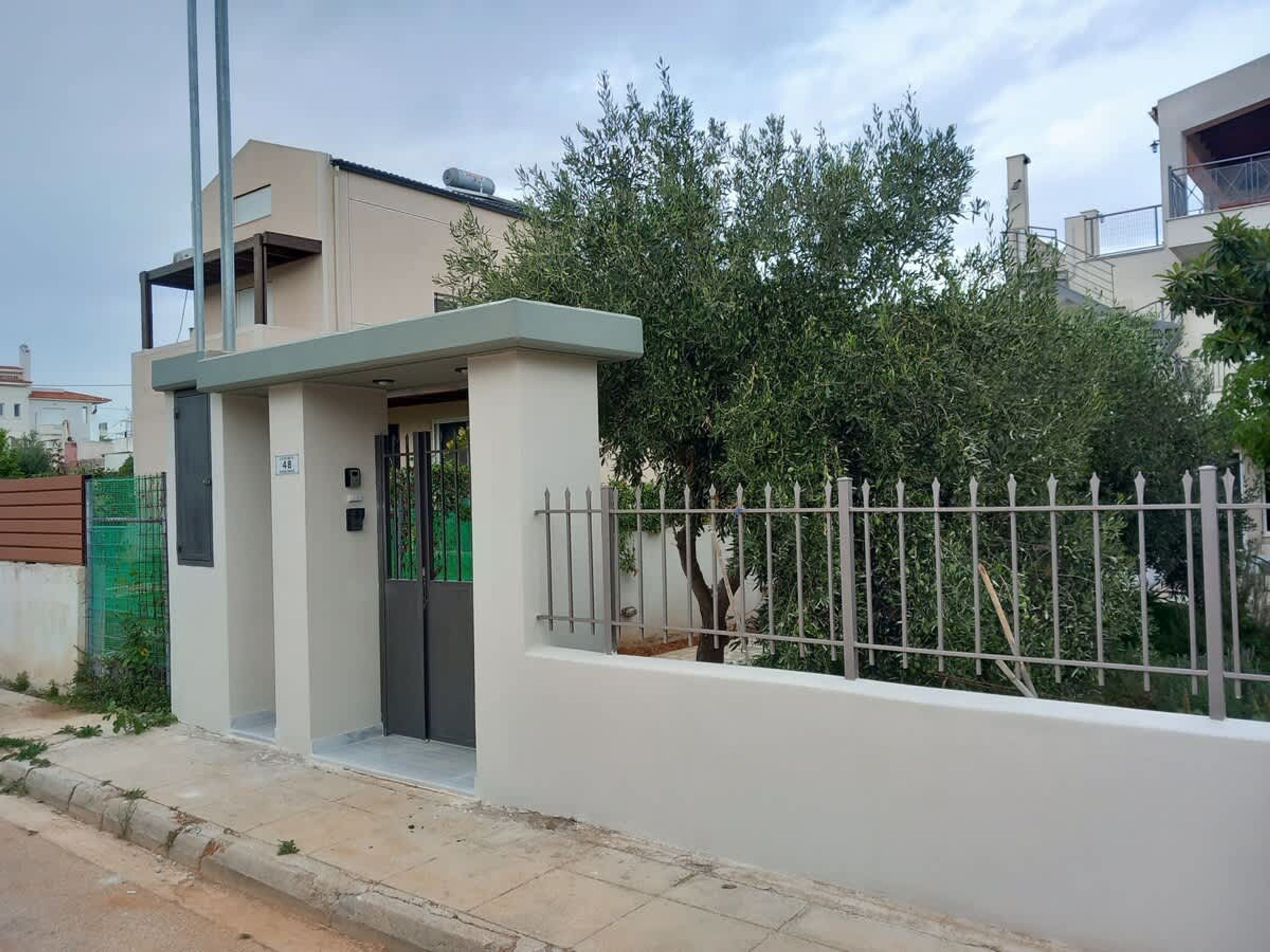 Una casa moderna con entrada protegida por un portón, un pequeño porche y cerca de metal.