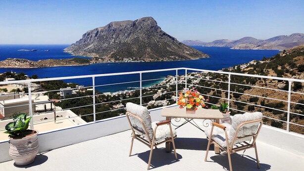 A balcony with a table and chairs, overlooking a coastal landscape with a prominent rocky island and a clear blue sea. - Escape to this Sea View Apartment close to Kalymnos Climbing Routes (KALYMNOS)