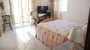 A bedroom with a bed, a desk with a television, a chair, and curtains. - Escape to this Sea View Apartment close to Kalymnos Climbing Routes (KALYMNOS)