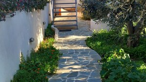 A stone pathway leading to a building entrance, surrounded by greenery and a metal gate. - Pavlos Loft Apartment - Leontari Garden Escape (Pallini)