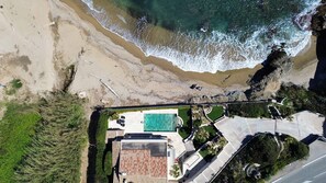Eine Luftaufnahme eines Küsteneigentums mit Swimmingpool, Terrasse und einer Straße, die zum Strand führt.
