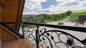 A wooden balcony with ornate black railing, overlooking a green landscape with a road and buildings. - Witowianka (Koscielisko)