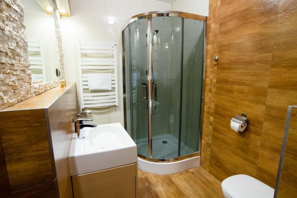 Un baño con ducha de vidrio, un lavamanos blanco y piso de madera.