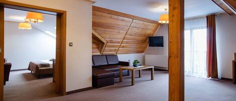 A room with a sloped ceiling, a sofa, a small table, and a television.