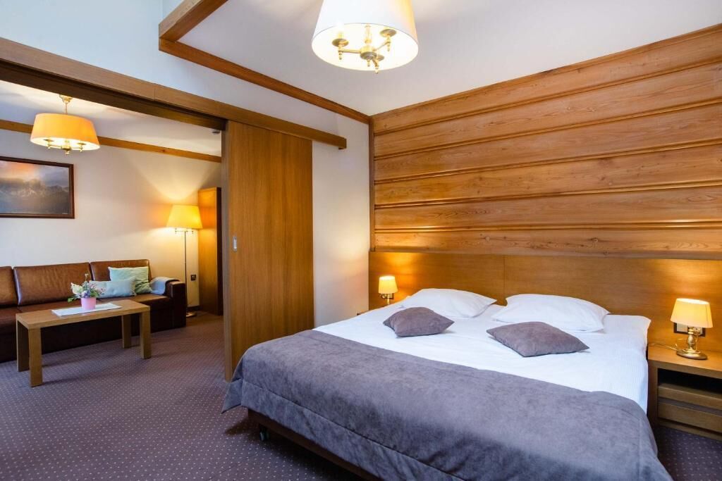A hotel room with a bed, bedside tables, a sofa, and a lamp.