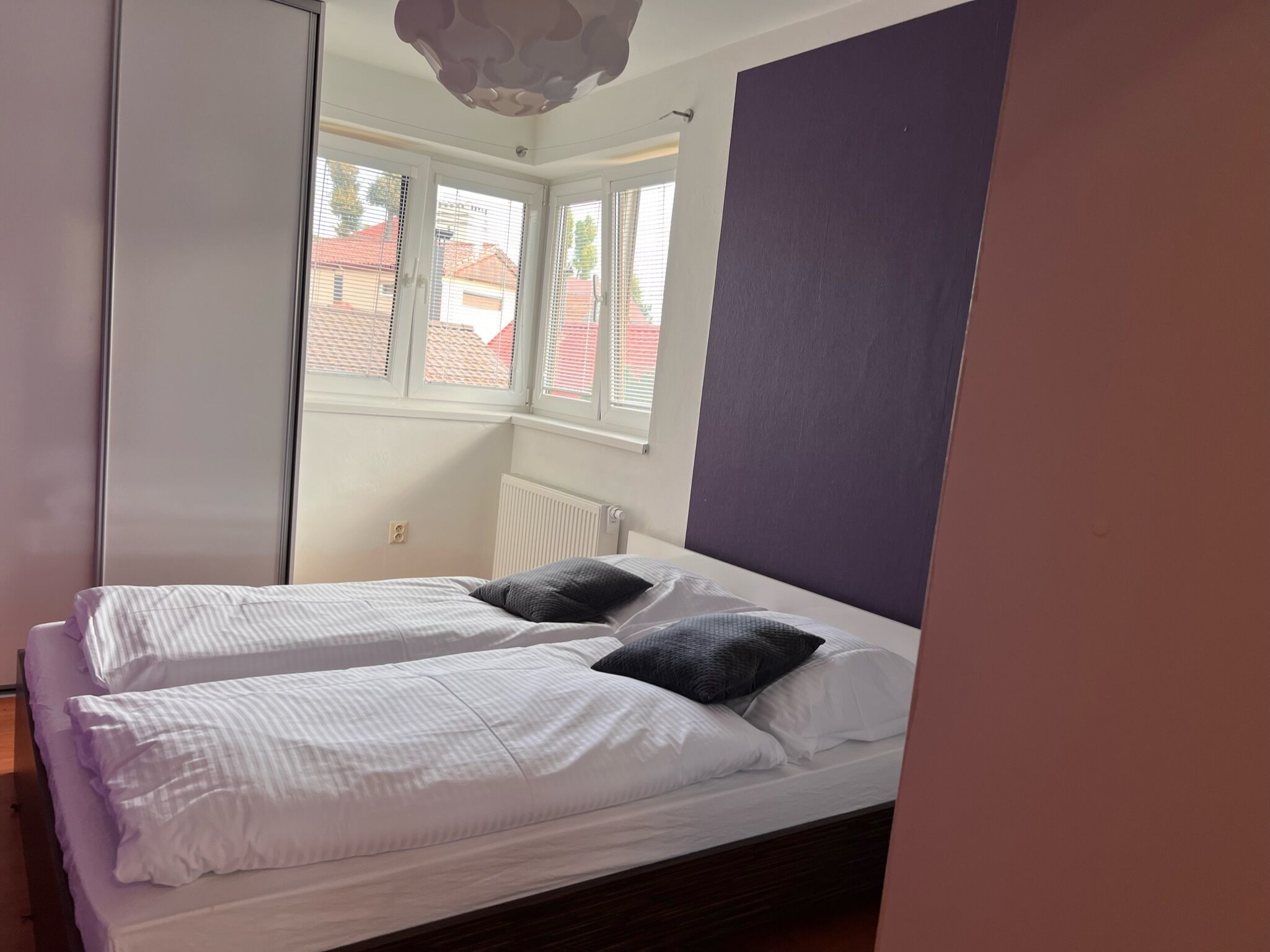 A bedroom with a bed, two pillows, a window, and a radiator.