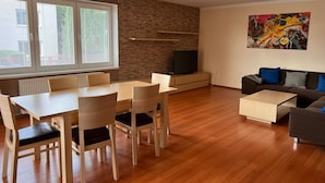 A modern living room with a dining table, chairs, a sofa, a TV, and a painting on the wall.