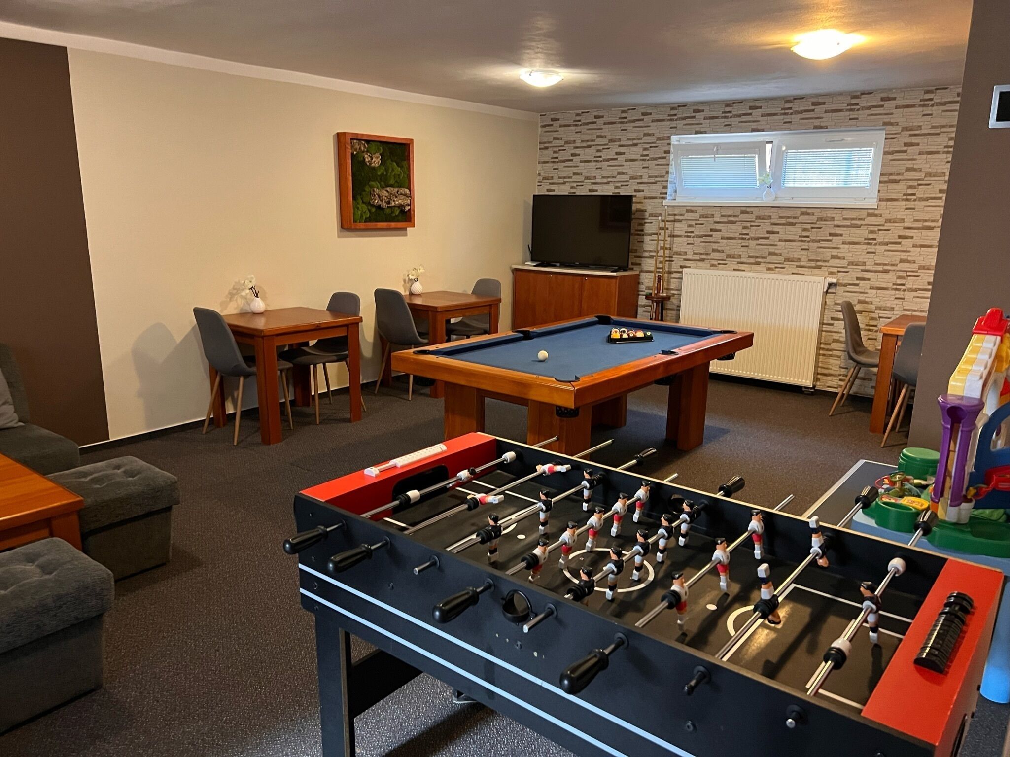 Una habitación con mesa de billar, mesa de futbolín, televisor y comedor con sillas y mesa.
