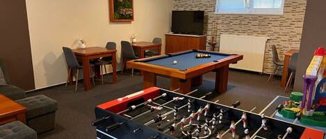 Una habitación con mesa de billar, mesa de futbolín, televisor y comedor con sillas y mesa.