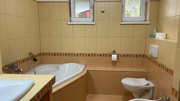 Une salle de bain avec une baignoire, des toilettes, un lavabo et deux fenêtres.