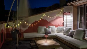 A cozy outdoor seating area with a sofa and cushions, a small table with a wine glass, string lights, and a wall mural. - BELLEROSE HOUSE IN HAMLET (Le Plan-de-la-Tour)