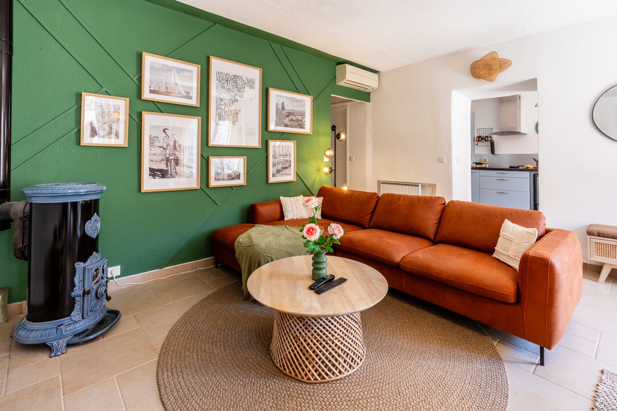 Un salon avec un mur d’accent vert, un canapé marron, une table basse ronde ornée d’un vase de fleurs et des tableaux encadrés accrochés au mur.
