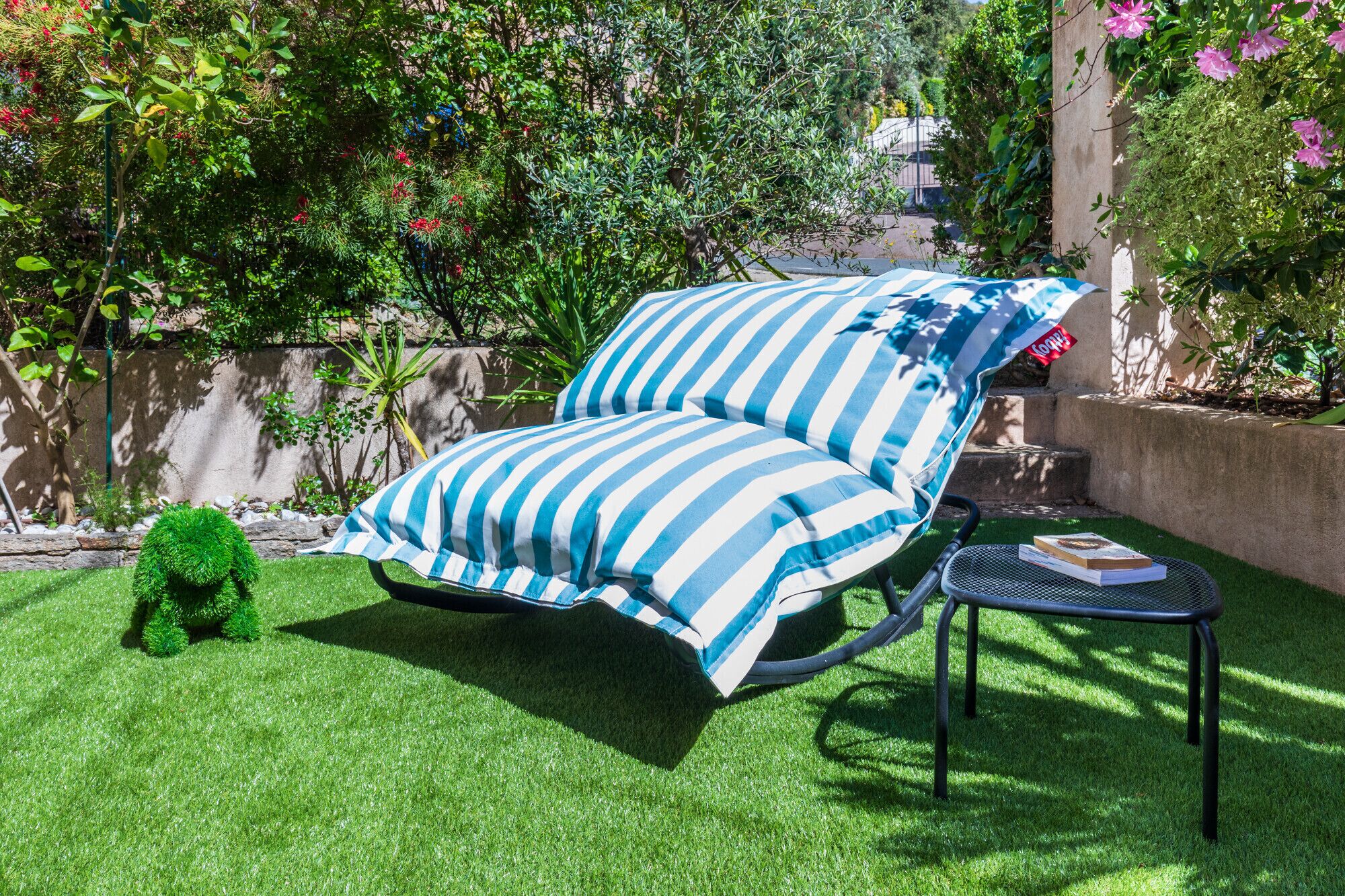 Una silla de relax con cojines a rayas, una pequeña mesa redonda con un libro y un césped bien cuidado.