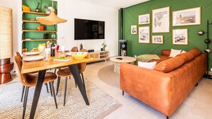 A living room with a green wall, a brown leather sofa, a dining table with chairs, a TV, and framed pictures. - BELLEROSE HOUSE IN HAMLET (Le Plan-de-la-Tour)
