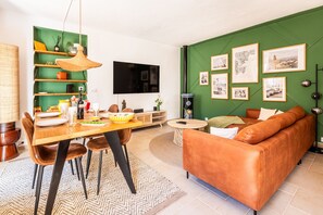 A living room with a green wall, a brown leather sofa, a dining table with chairs, a TV, and framed pictures. - BELLEROSE HOUSE IN HAMLET (Le Plan-de-la-Tour)
