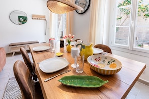 A dining table set with plates, glasses, and a pitcher, with a chair and a bench in the background. - BELLEROSE HOUSE IN HAMLET (Le Plan-de-la-Tour)