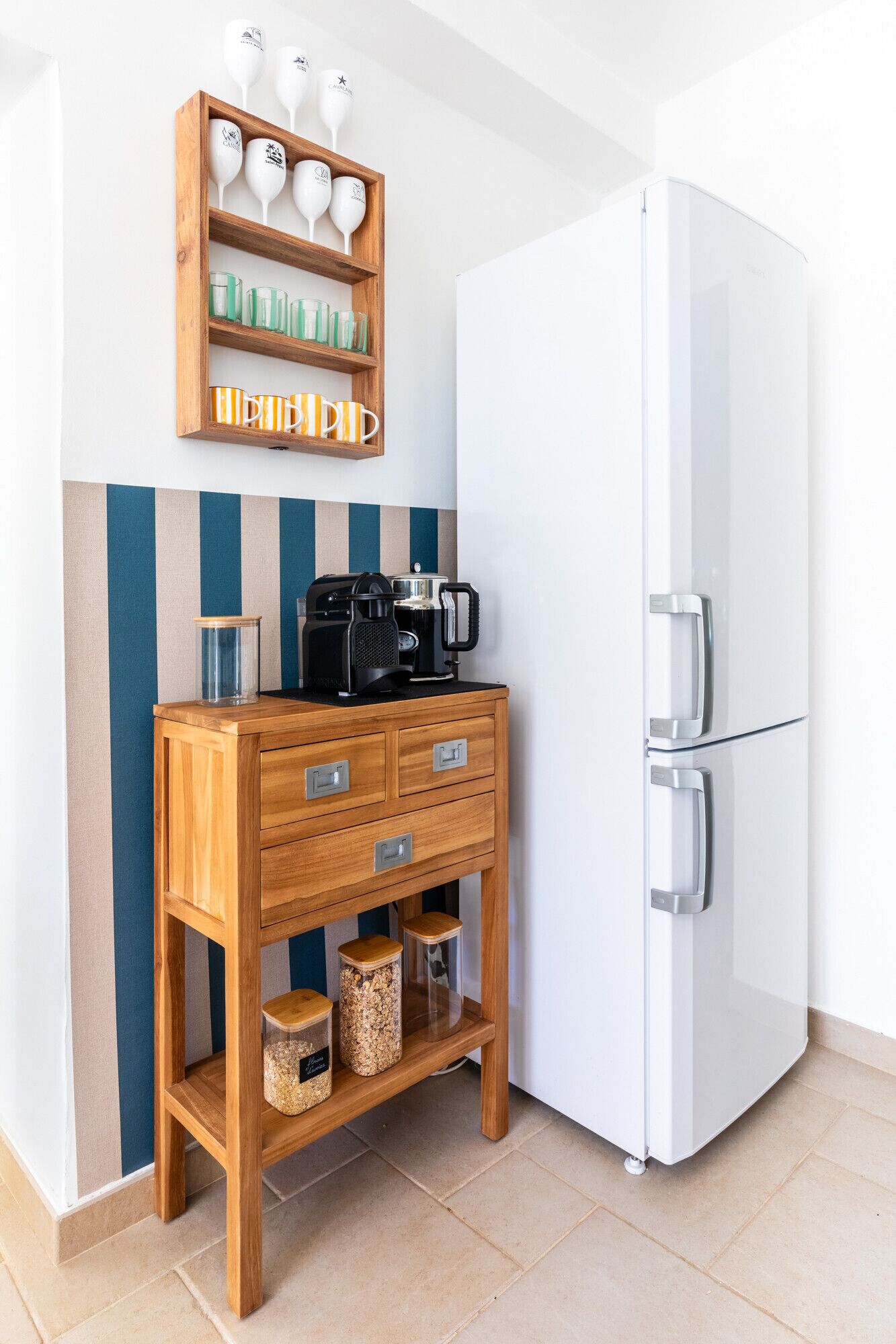 A kitchen with a white refrigerator, wooden cabinet with drawers, and a shelf with glass jars.