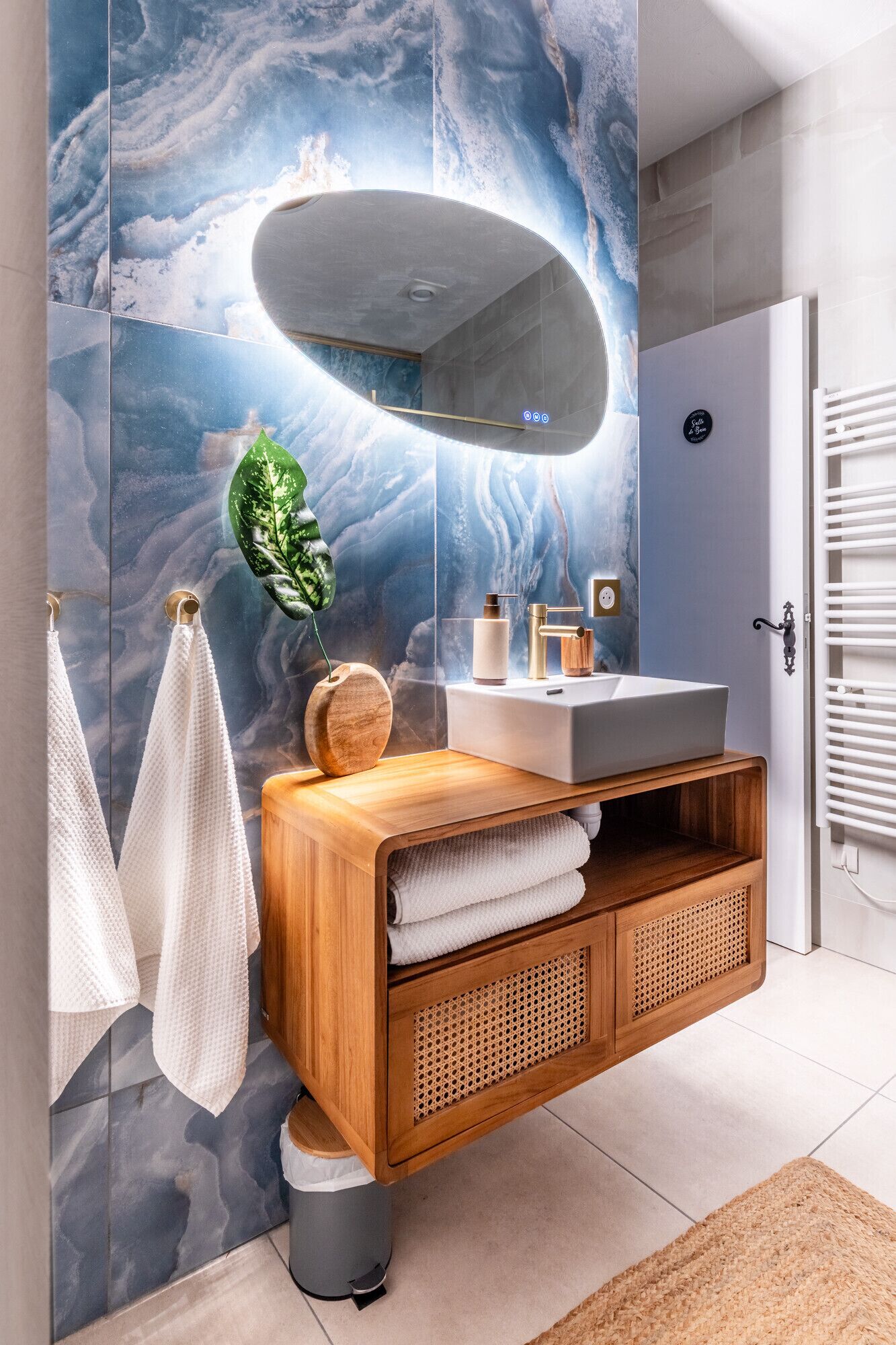 Une salle de bain moderne avec un mur en marbre, un meuble-lavabo en bois, un grand miroir et un porte-serviettes.
