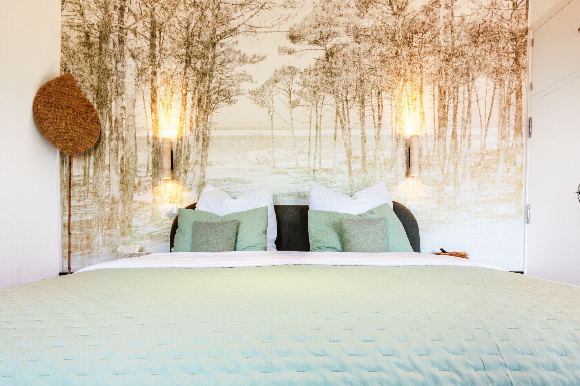 Un dormitorio con cama, almohadas, un tapiz de pared y dos luces fijadas a la pared.