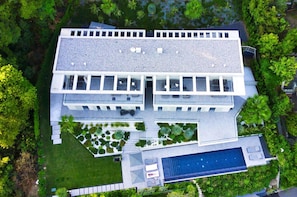 Un edificio moderno con piscina en la azotea, rodeado de abundante vegetación.