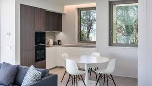 A modern kitchen with dark wood cabinets, a white dining table with four chairs, and a large window with a view of trees. - Villa 'Acquariva Luxury and Privacy' with Lake View, Wi-Fi and Air Conditioning (Salò)
