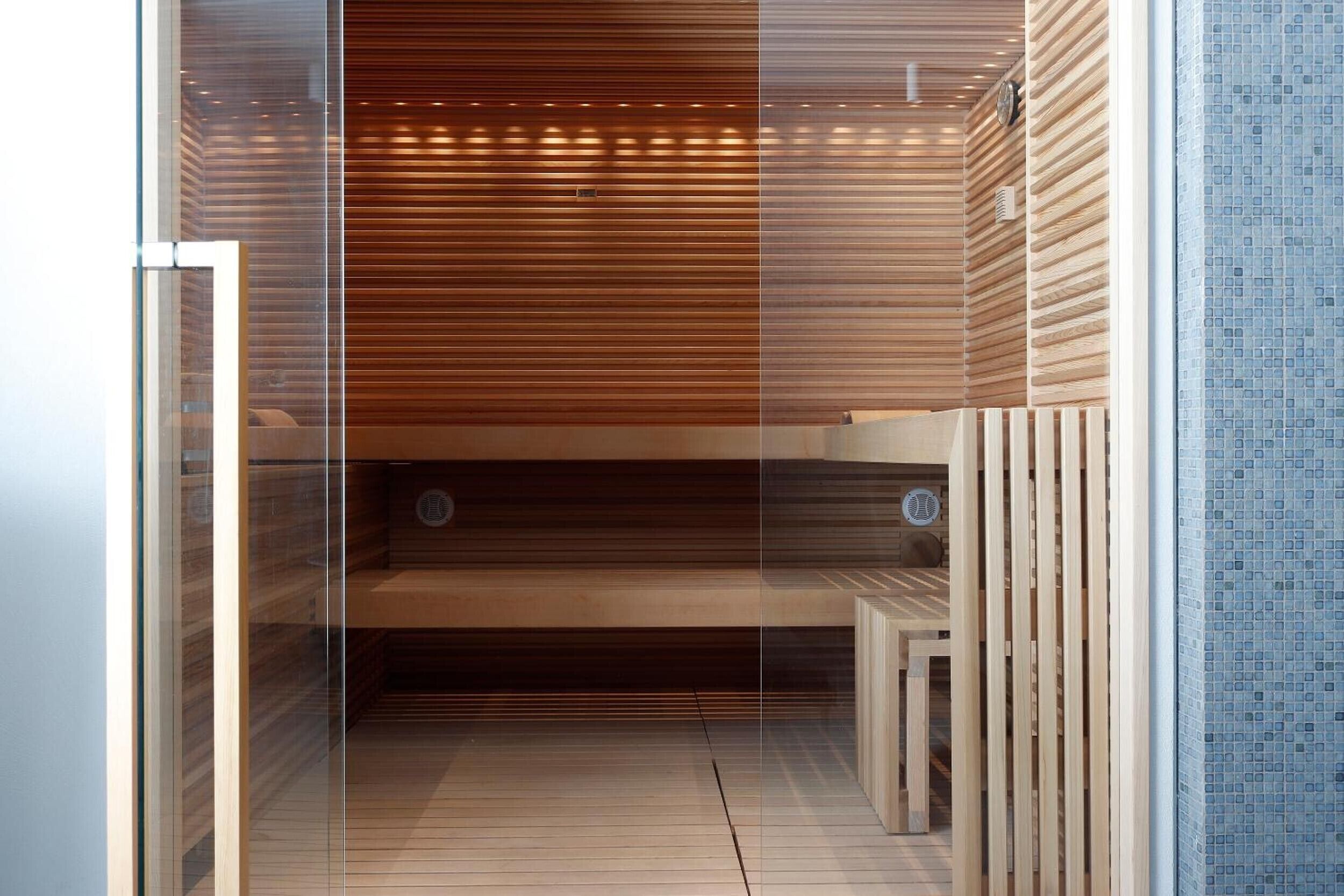 Una sauna moderna con listones de madera, un panel de vidrio y una pared de azulejos.