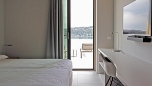 A hotel room with a bed, a desk, a chair, and a view of a cityscape through a large window. - Villa 'Acquariva Luxury and Privacy' with Lake View, Wi-Fi and Air Conditioning (Salò)