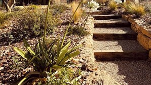 Una casa con tetto in tegole, un giardino con diverse piante e un vialetto in pietra che conduce all'ingresso.