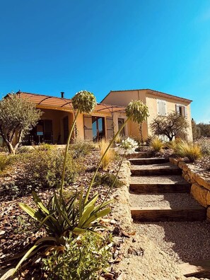 A house with a tiled roof, a garden with various plants, and a stone pathway leading to the entrance. - Mas de la Canopée, pool & air condition (Saint-Saturnin-lès-Apt)