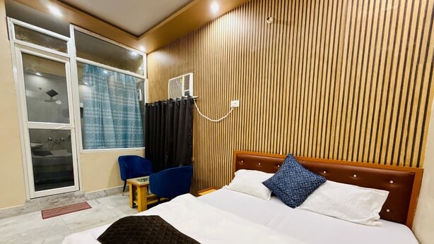 Ein Hotelzimmer mit Bett, Sessel, kleinem Tisch, Heizung und einem Fenster mit Vorhängen.