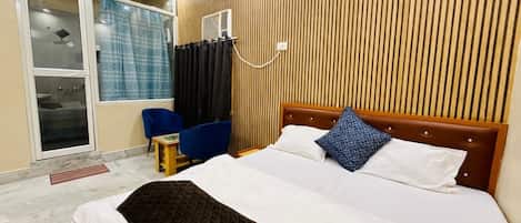 Una habitación de hotel con cama, una silla, una mesita, un calefactor y una ventana con cortinas.