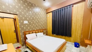 Ein Hotelzimmer mit einem Bett, einer Holztür, einem Fenster mit Vorhängen, einem kleinen Tisch und einem blauen Eimer.