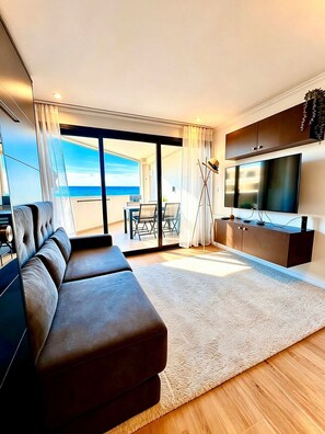 Ein modernes Wohnzimmer mit einer Couch, einem Flachbildfernseher und Blick aufs Meer.