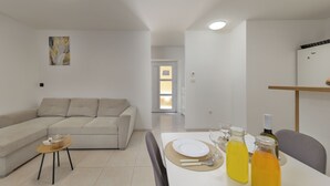 A modern living room with a sofa, a dining table set with glassware and bottles, and a painting on the wall. - Casa Valdebek With Pool (Pula)