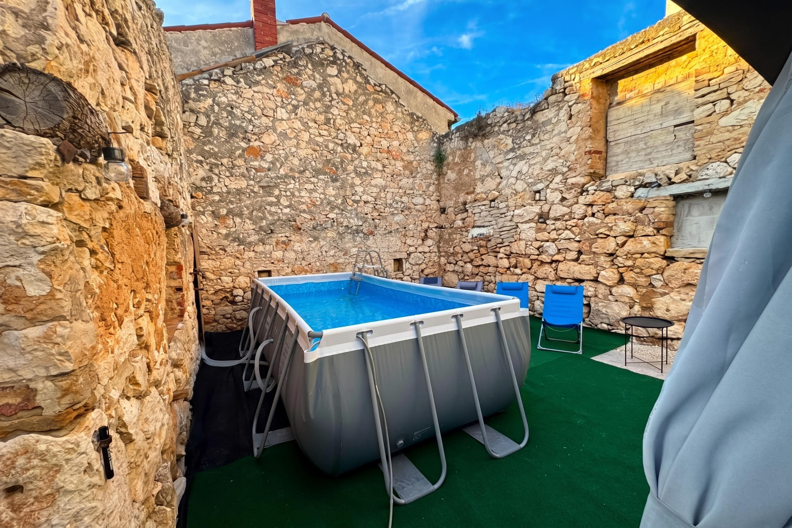 Une cour bordée de murs en pierre, avec une piscine rectangulaire, une échelle et des sièges d’extérieur.