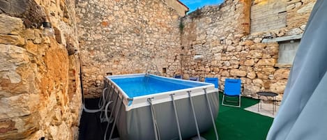 Une cour bordée de murs en pierre, avec une piscine rectangulaire, une échelle et des sièges d’extérieur.