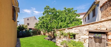 A narrow courtyard with a well-maintained lawn, stone walls, and a variety of plants.