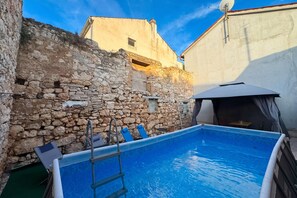 A swimming pool with a ladder, surrounded by stone walls and a building with a satellite dish. - Casa Valdebek With Pool (Pula)