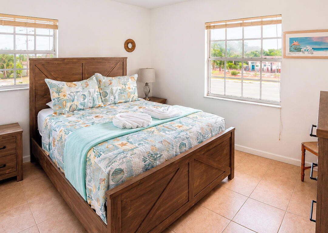 Un dormitorio con cama de madera, una mesita de noche, una lámpara, una ventana con vistas y una silla.