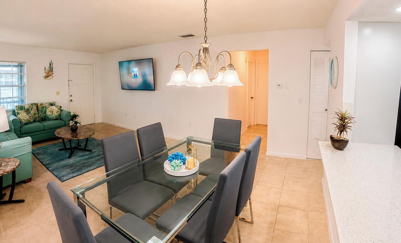 Una sala de estar moderna con una mesa de comedor de vidrio, sillas grises, un sofá verde y un televisor montado en la pared.