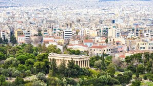 Panoramica urbana con un imponente tempio greco antico, circondato da edifici e aree verdi.