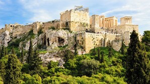 Un'antica fortezza in pietra con colonne storiche, una scala che conduce ai livelli superiori e un lussureggiante paesaggio verde circostante.