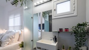 Un bagno moderno con cabina doccia in vetro, un mobile lavabo bianco con specchio e un letto con biancheria da letto bianca.