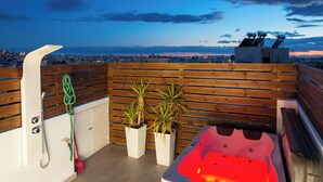Una terrazza sul tetto con idromassaggio, pavimento in legno, piante in vaso e vista sulla città.