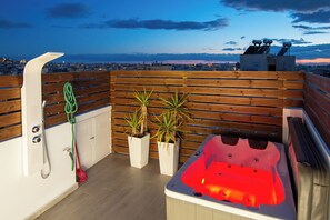 Eine Dachterrasse mit Whirlpool, Holzboden, Topfpflanzen und Blick auf die Stadt.