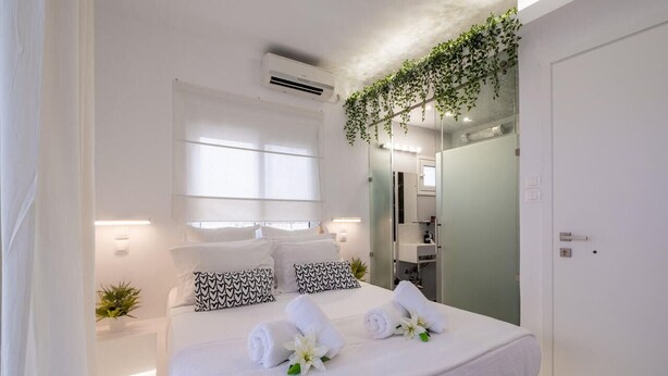 Una camera d'albergo moderna con un letto grande, lenzuola bianche, uno specchio e una piccola pianta.