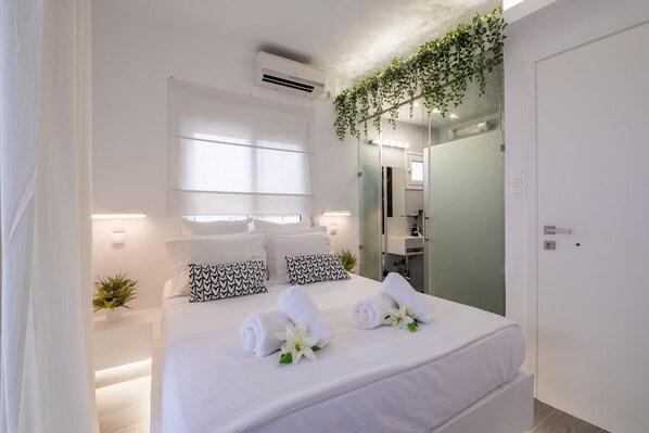 Ein modernes Hotelzimmer mit einem großen Bett, weißen Laken, einem Spiegel und einer kleinen Pflanze.