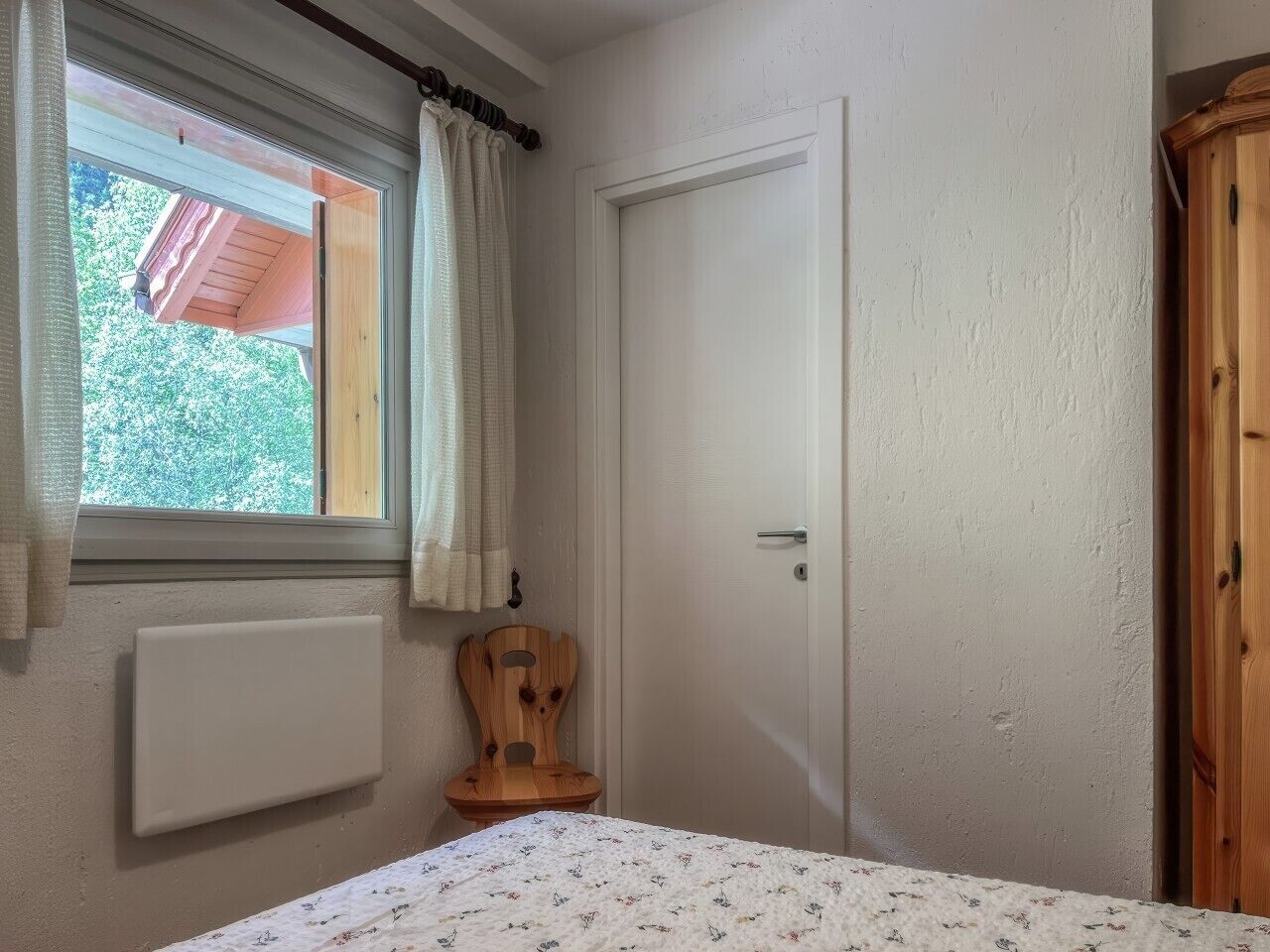 Ein Schlafzimmer mit Fenster, Heizkörper, Holzstuhl und Kleiderschrank.