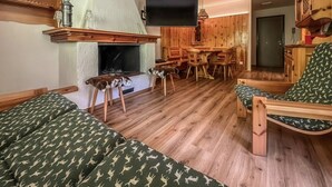A cozy living room with a fireplace, wooden furniture, a television, and a dining area. - Casa Castoro - In the heart of Val di Peio (Peio Fonti)